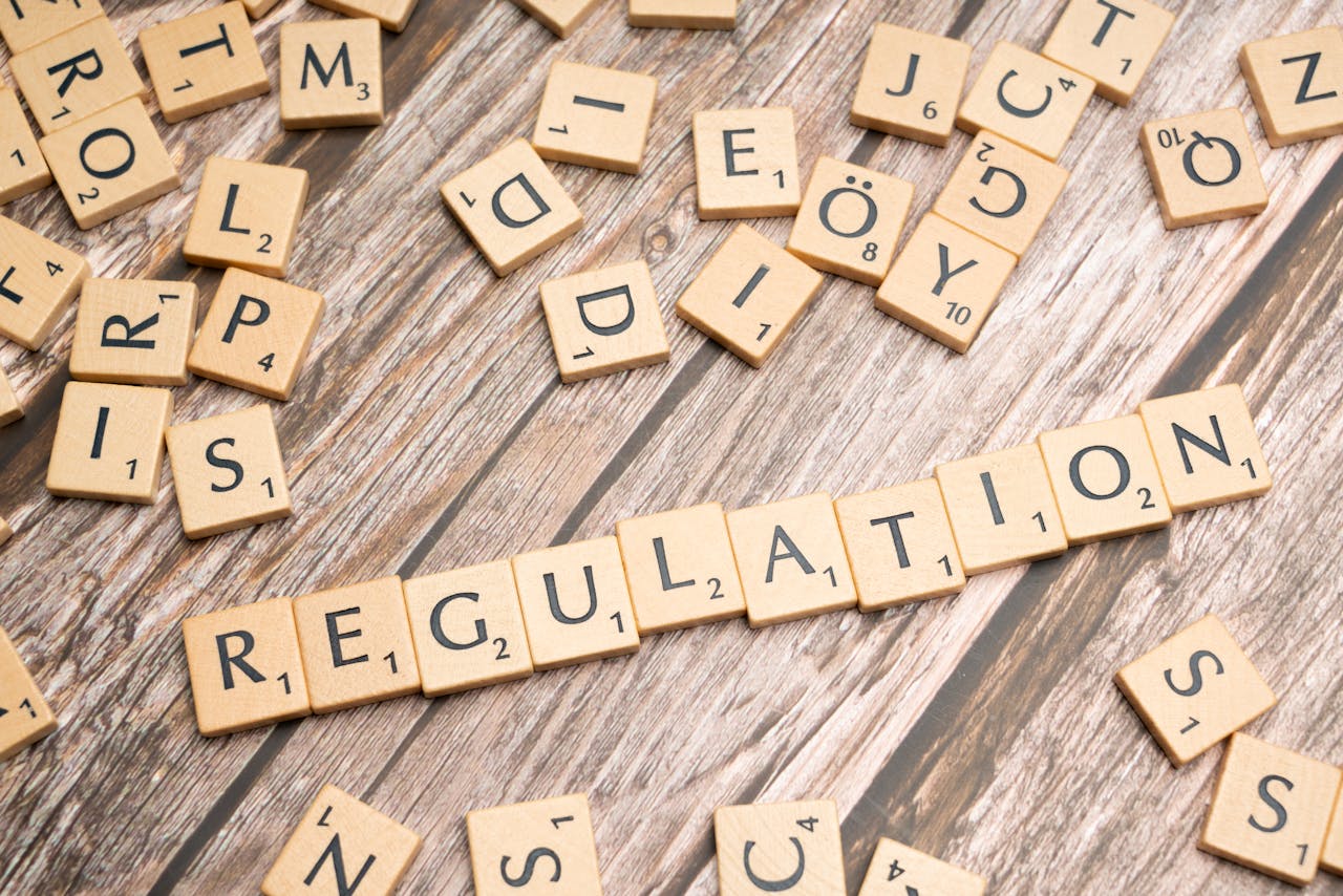 Wooden letter tiles spelling Regulation on a textured wood background, conveying themes of compliance and structure.